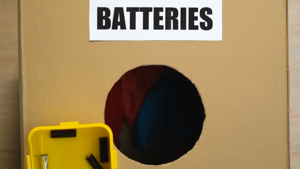 Mão jogando baterias na caixa com roupas na parte inferior, classificação inadequada — Vídeo de Stock