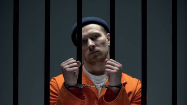 Parmaklıkların arkasında duran ve el kelepçeli elleri gösteren tehlikeli kibirli mahkum