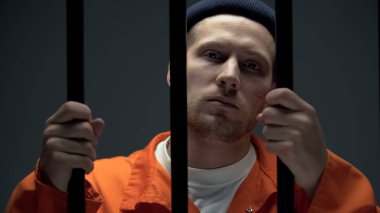 Ağlayan mahkum parmaklıkları tutuyor ve kameraya bakıyor, kendini suçlu ve çaresiz hissediyor.