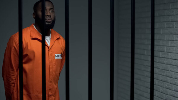 Indifferent afro american prisoner praying to god in cell, waiting for sentence