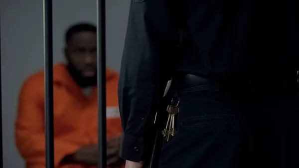 細胞の中のアフロ アメリカンの監禁される男性を見ている鍵を持つセキュリティ ウォーデン — ストック写真