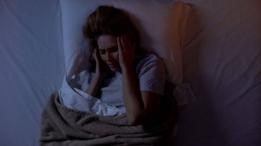 Genç bayan yatakta başını tutarak, gece uyandıktan sonra baş ağrısı acı