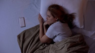 Yatakta yatan yalnız bayan, akıllı telefona bakıyor, erkek arkadaşından sms bekliyor