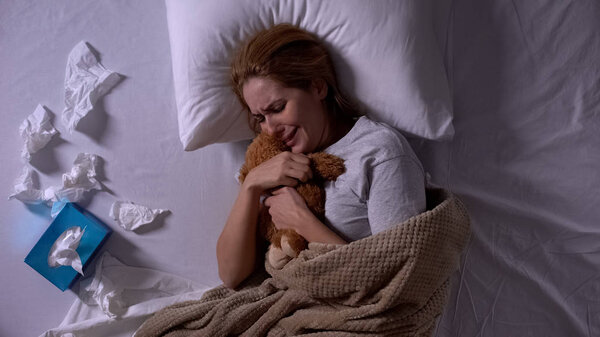 Девушка в постели плачет, обнимает плюшевого мишку, чувствует депрессию и разочарование
