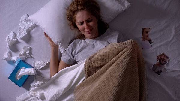 Женщина плачет лежа в постели с салфетками, разорванная фотография бывшего парня рядом, перерыв
