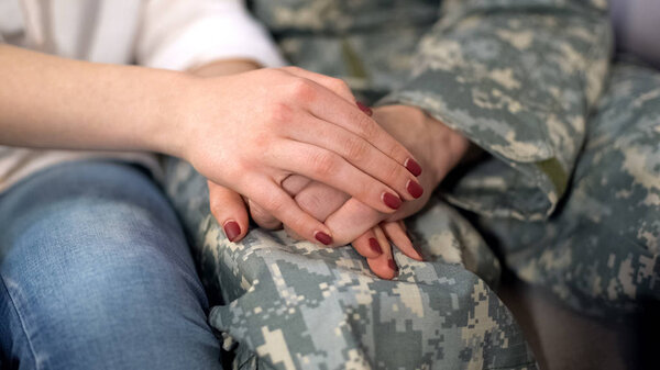 Military man and girlfriend holding hands, supporting boyfriend before leaving