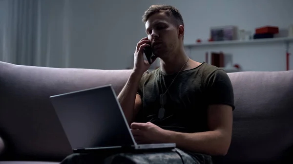 男性の軍のスパイは ソファの上にラップトップで座って 夜にスマートフォンを話す — ストック写真