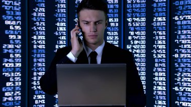Takım elbiseli adam dizüstü bilgisayar üzerinde çalışıyor, telefona cevap, finansal piyasa verileri, hisse senedi