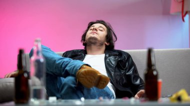 Kanepede dinlenen sarhoş genç adam, masada alkol şişeleri, öğrenci partisi