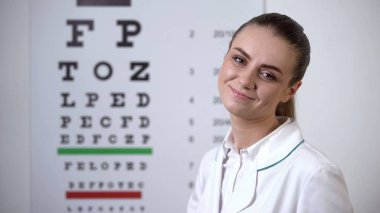 Profesyonel görme kliniğinde göz grafiğine yakın poz veren gülümseyen göz doktoru