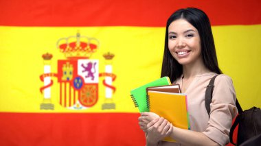 Neşeli Asyalı kız öğrenci İspanyol bayrağına karşı ayakta, dil eğitimi