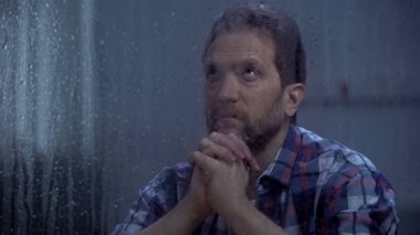 Umutsuz erkek yağmurlu pencerearkasında Tanrı dua, yardım ve af isteyen