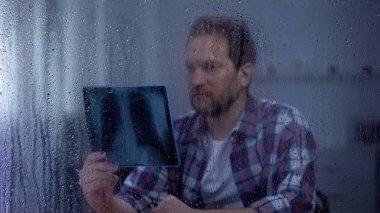 Üzgün adam akciğerler x-ray, ölümcül hastalık, iyileşme için hiçbir umut, yağmurlu gün bakıyor