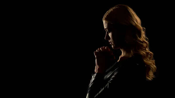 Blond woman praying in dark place, asking for forgiveness, sinner confession