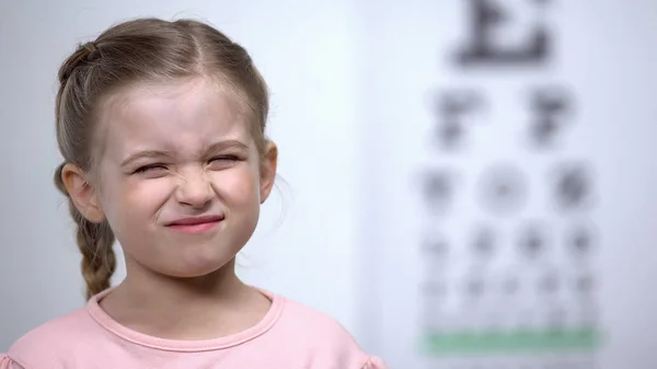 小女孩皱着眉头 试图看到信在视觉测试表模糊视力 — 图库照片