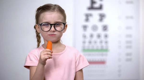 可爱的女孩在眼镜咀嚼胡萝卜 维生素A良好的视力 医疗保健 — 图库照片