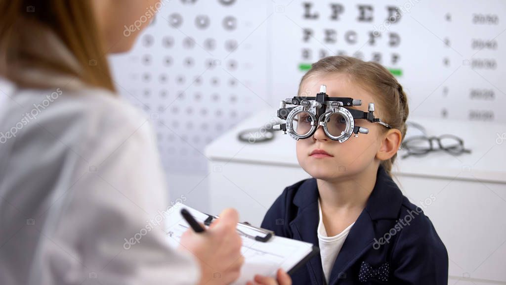 Cute girl in optical trial frame waiting prescription from ophthalmologist