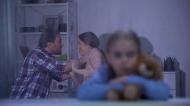 Yağmurlu günde oyuncak ayıya sarılan kız, baba anneyi arka planda boğuyor