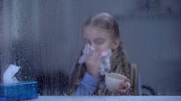 Mała Dziewczynka Cierpiąca Grypę Deszczowe Okno Kichanie Trzymając Filiżankę Herbaty — Zdjęcie stockowe