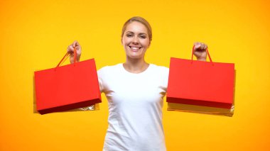 Turuncu arka planda alışveriş çantaları gösteren gülümseyen güzel bayan, tatil satış