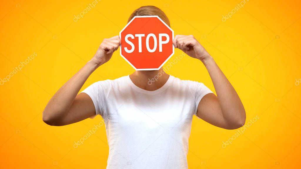 Young woman holding red stop sign front face, negative reaction, warning problem