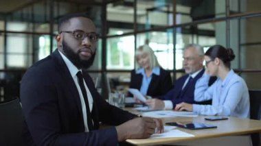Takım elbise li ve gözlüklü siyah erkek yönetici kamera oturma toplantı odası arıyor