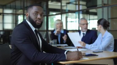 Afrikalı ofis çalışanı kamera görünümlü, iş ortakları arka planda konuşuyor