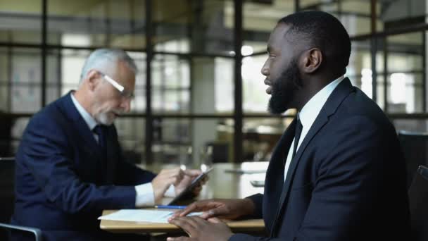 Mature business man refusing african job candidate reading resume on tablet — Stock Video