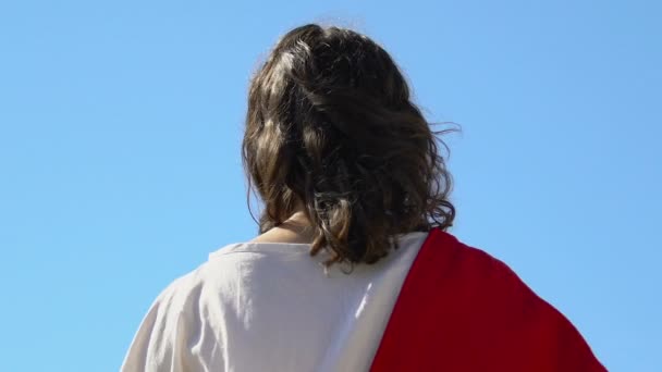 Jesus Cristo de roupão segurando cruz e levantando as mãos para o céu, vista para trás — Vídeo de Stock