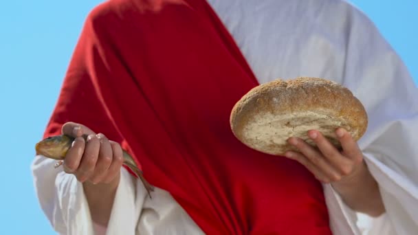 Монах в халате держит рыбу и хлеб, дары с небес, знак Иисуса Христа — стоковое видео