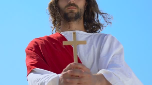 Иисус в мантии показывает деревянный крест перед камерой, символ христианской религии, крупный план — стоковое видео