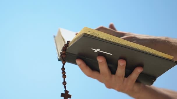 Manos masculinas sosteniendo la Biblia con rosario, sacerdote rezando celebrando misa, bautismo — Vídeos de Stock