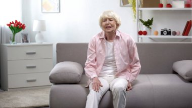 Kanepede oturan yaşlı kadın diz ağrısı hissi, travma sonrası rehabilitasyon