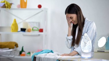 Üzgün ev kadını ütü leme sırasında başını tutarak, zor ev iş sonra yorgun