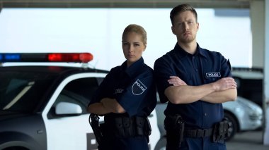 Kendinden emin erkek ve kadın polis memurları devriye arabasının yanında duruyor