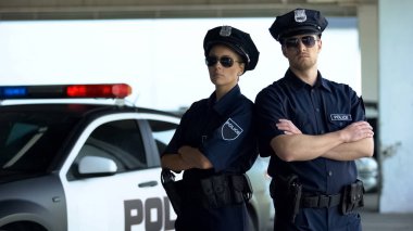 Devriye arabasına karşı duran üniforma lı ve güneş gözlükli kendinden emin polis takım arkadaşları