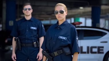 Ciddi kadın ve erkek polis memurları güneş gözlüğü açık, güvenlik ayakta