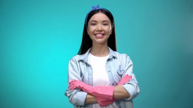 Elleri çapraz duran ve kameraya gülümseyen eldivenler içinde kendine güvenen ev hanımı