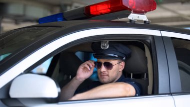 Devriye arabasında oturan güneş gözlüklerini ayarlayan genç polis, sorumlu iş