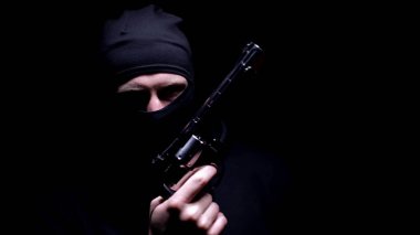 Balaclava maskeli tehlikeli adam silah tutuyor, siyah arka plan, seri katil