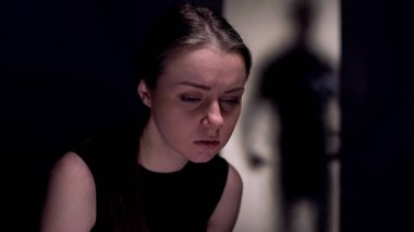 Üzgün kadın aşağı bakıyor, tehlikeli adam kapıya gölge, insan ticareti kurbanı