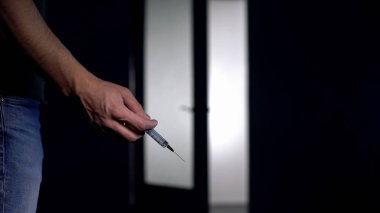 Adam elinde şırınga, uyuşturucu bağımlılığı kavramı, siyah arka plan, aşırı doz riski