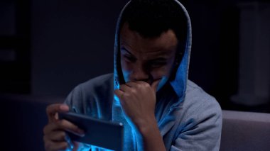 Sıkılmış afro-amerikan genç karanlık odada akıllı telefon kaydırma, uykusuz