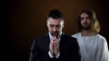 Dua eden işadamı el ele tutuşuyor, mesih arkada duruyor, manevi destek