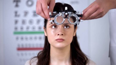 Göz doktoru korkmuş kadın hastaya refraktör koyarak, görme yetisini analiz