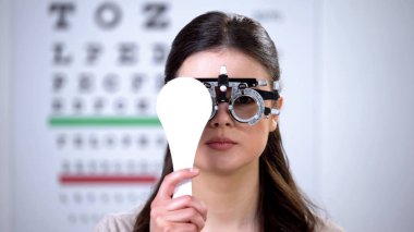 Girl in refractor closing one eye, ophthalmologist appointment, vision check-up clipart