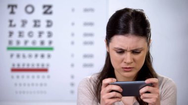 Akıllı telefonda video oyunu oynayan bağımlı kadın, görme üzerinde zararlı etkisi