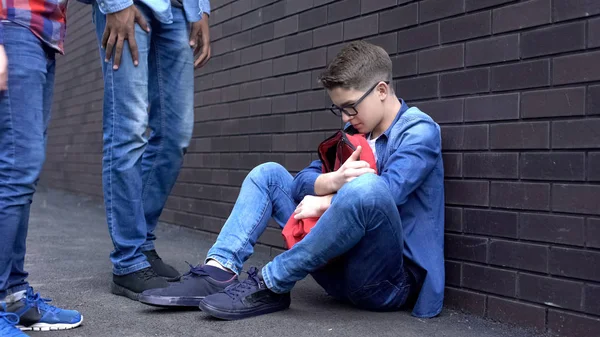 Duvara yaslanmış genç çocuk, kabadayı öğrencilerden korkuyor, okulda gözdağı