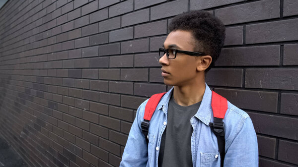 Scared black boy leaning against wall, intimidated victim of racial bullying