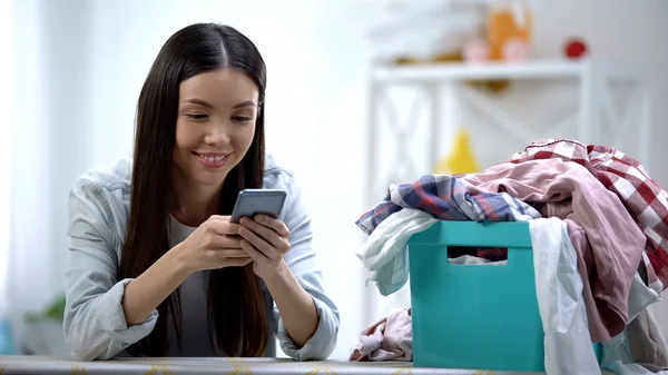 Χαμογελαστή Νοικοκυρά Συνομιλεί Στο Smartphone Κοντά Στο Καλάθι Πλυντηρίων Ρούχα — Φωτογραφία Αρχείου